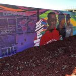 Portion of Teralta Park Unity mural featuring a the City Heights Library, a stack of books, and three men.