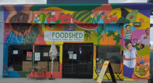 Storefront mural depicting gardening, produce, and people enjoying healthy food.