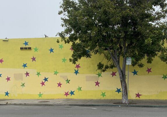 Urban wall mural featuring many colorful stars on a yellow background.